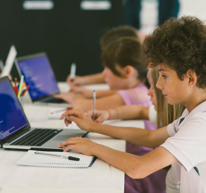 Group of children sitting in a row at the table while they use their laptops