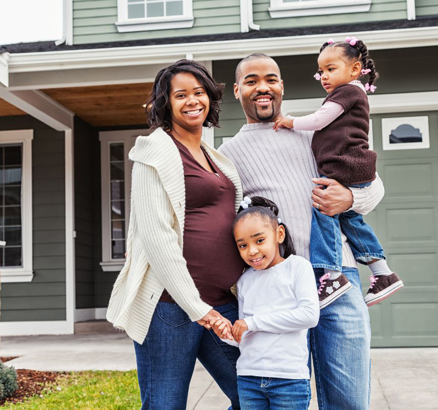 Family of 2 adults and 2 children smiling in front of their house