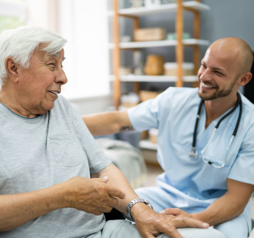 Smiling caregiver comforts smiling older man in a medical setting